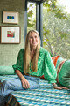Portrait of Lauren Elliot seated on a vibrant window seat styled with Christopher Farr Cloth fabrics and trims, showcasing her distinctive colourful and textured design aesthetic.